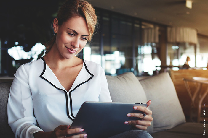 Frau sitzt entspannt auf einem Sofa und nutzt ein Tablet zur digitalen Katalogansicht.