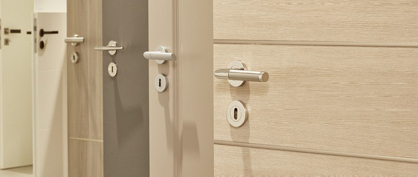 Mehrere nebeneinander angeordnete Türblätter in unterschiedlichen Farbtönen (weiß, holzähnlich, grau) mit integrierten Türgriffen.