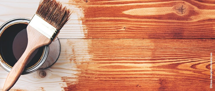 Eine geöffnete Dose Glasur neben einem Pinsel, der auf einer teilweise bemalten Holzoberfläche liegt.