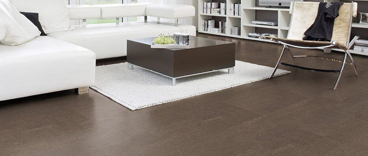 Der Boden im Wohnzimmer ist mit schokoladenfarbenem Kork ausgelegt. Weiter hinten stehen ein Sofa, ein Couchtisch und ein Sessel.