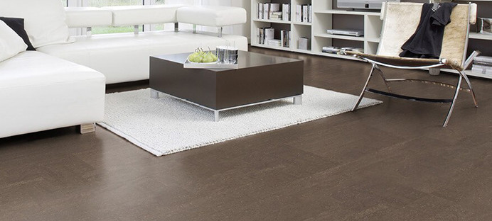 Der Boden im Wohnzimmer ist mit schokoladenfarbenem Kork ausgelegt. Weiter hinten stehen ein Sofa, ein Couchtisch und ein Sessel.