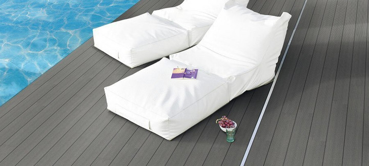 Graue WPC-Terrasse neben einem Pool mit zwei weißen Sonnenliegen.