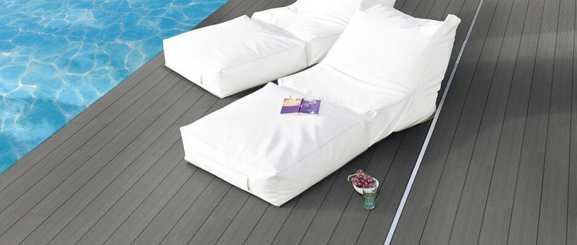 Graue WPC-Terrasse neben einem Pool mit zwei weißen Sonnenliegen.