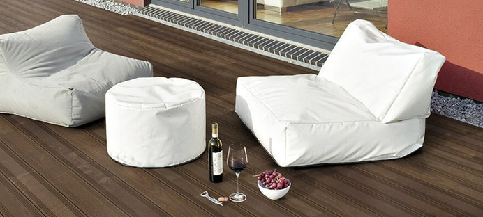 Dunkle Holzterrasse neben einem Gebäude mit zwei Sitzkissen und dekorativen Elementen.