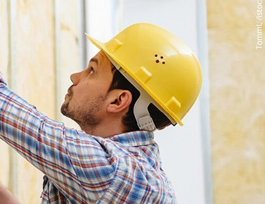 Handwerker mit gelbem Schutzhelm montiert eine Gipskartonplatte auf eine Metallständerwand mit Dämmung.